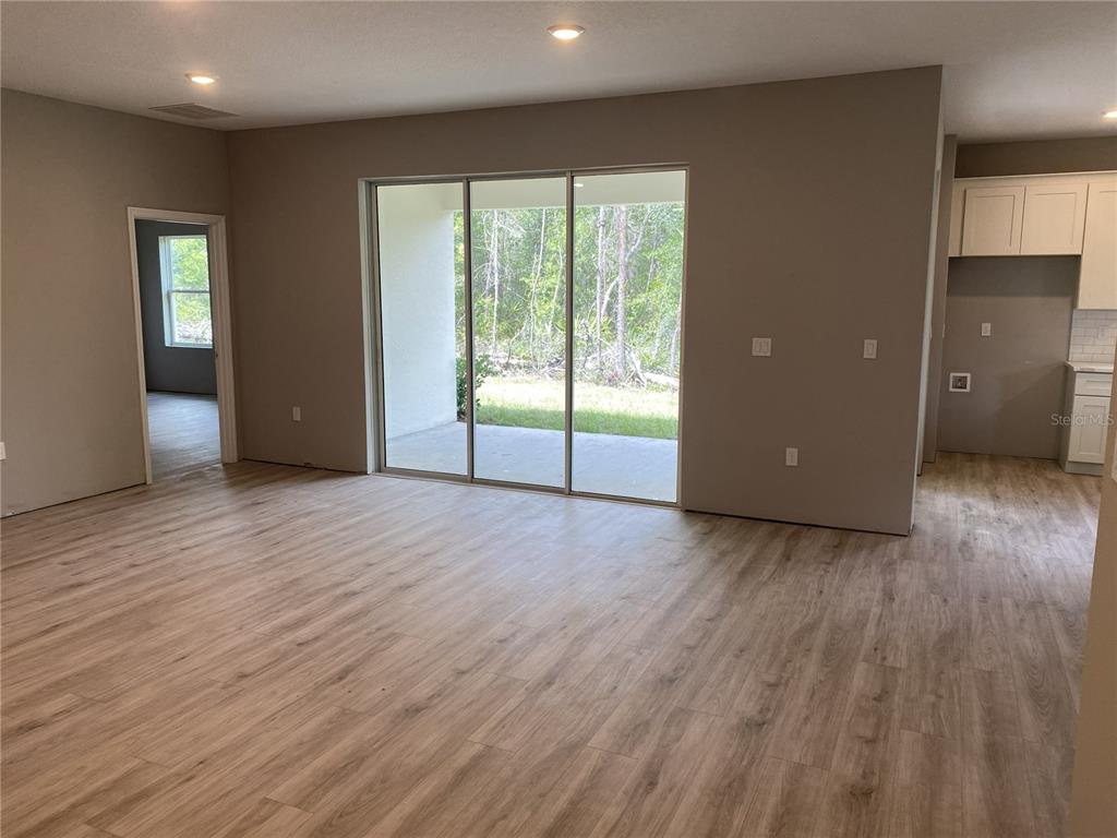 An open-concept living area features light wood-look flooring, recessed lighting, and sliding glass patio doors — 8362 NIGHTINGALE ROAD, SPRING HILL, FL