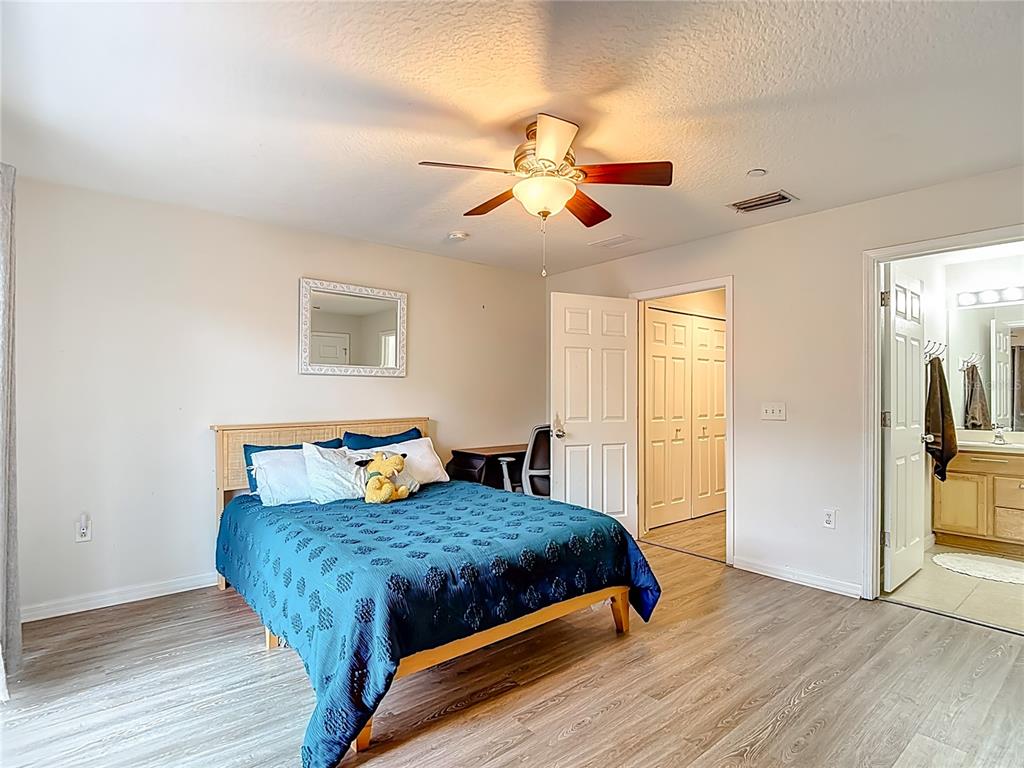 A bedroom features a blue bedspread, a ceiling fan, wood-look flooring, and an attached bathroom — 2426 MIDDLETON GROVE DRIVE, BRANDON, FL