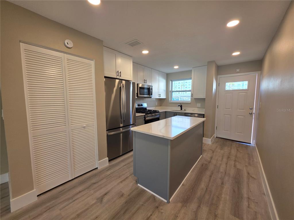 A kitchen features white cabinets, stainless steel appliances, a gray island, and light wood flooring — 6025 SHORE BOULEVARD S UNIT 105, GULFPORT, FL