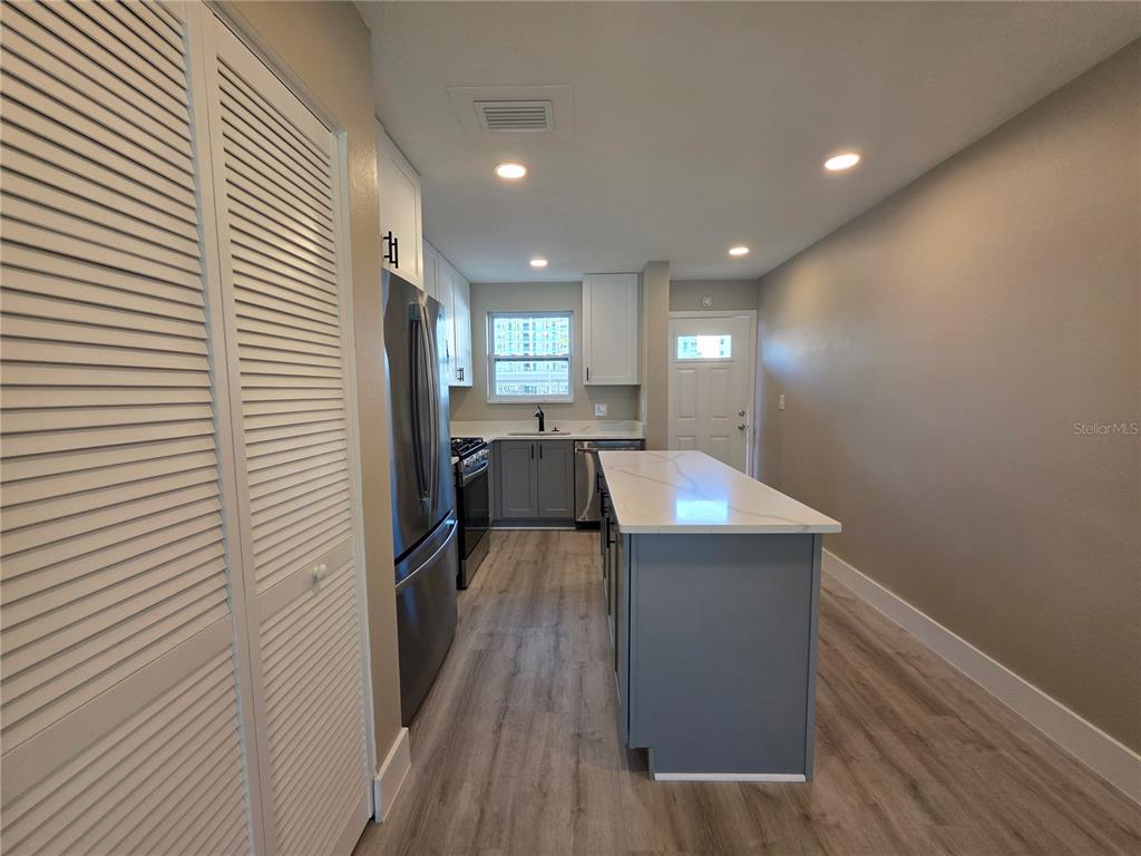 A kitchen features gray lower cabinets, white upper cabinets, a central island, and wood-look flooring — 6025 SHORE BOULEVARD S UNIT 105, GULFPORT, FL