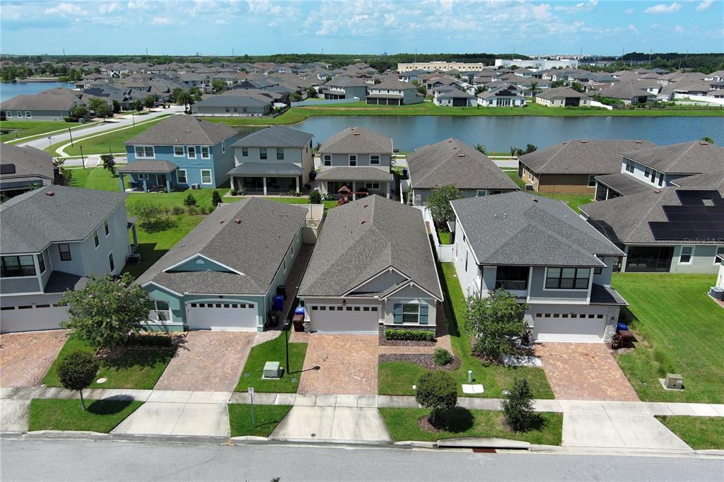 An aerial view shows a row of suburban houses with paved driveways and a nearby lake — 2480 VARENNA LOOP, KISSIMMEE, FL