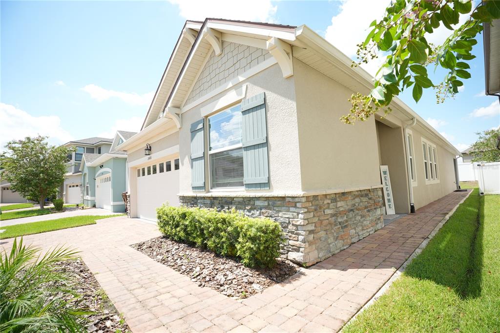 A beige single-story house with a stone facade, blue shutters, and a brick paver driveway — 2480 VARENNA LOOP, KISSIMMEE, FL