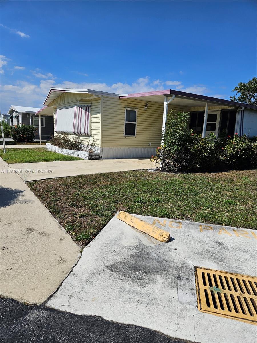 A light yellow mobile home features a covered porch and a concrete driveway — 109 NW 51st St, Deerfield Beach FL 33064, DEERFIELD BEACH, FL