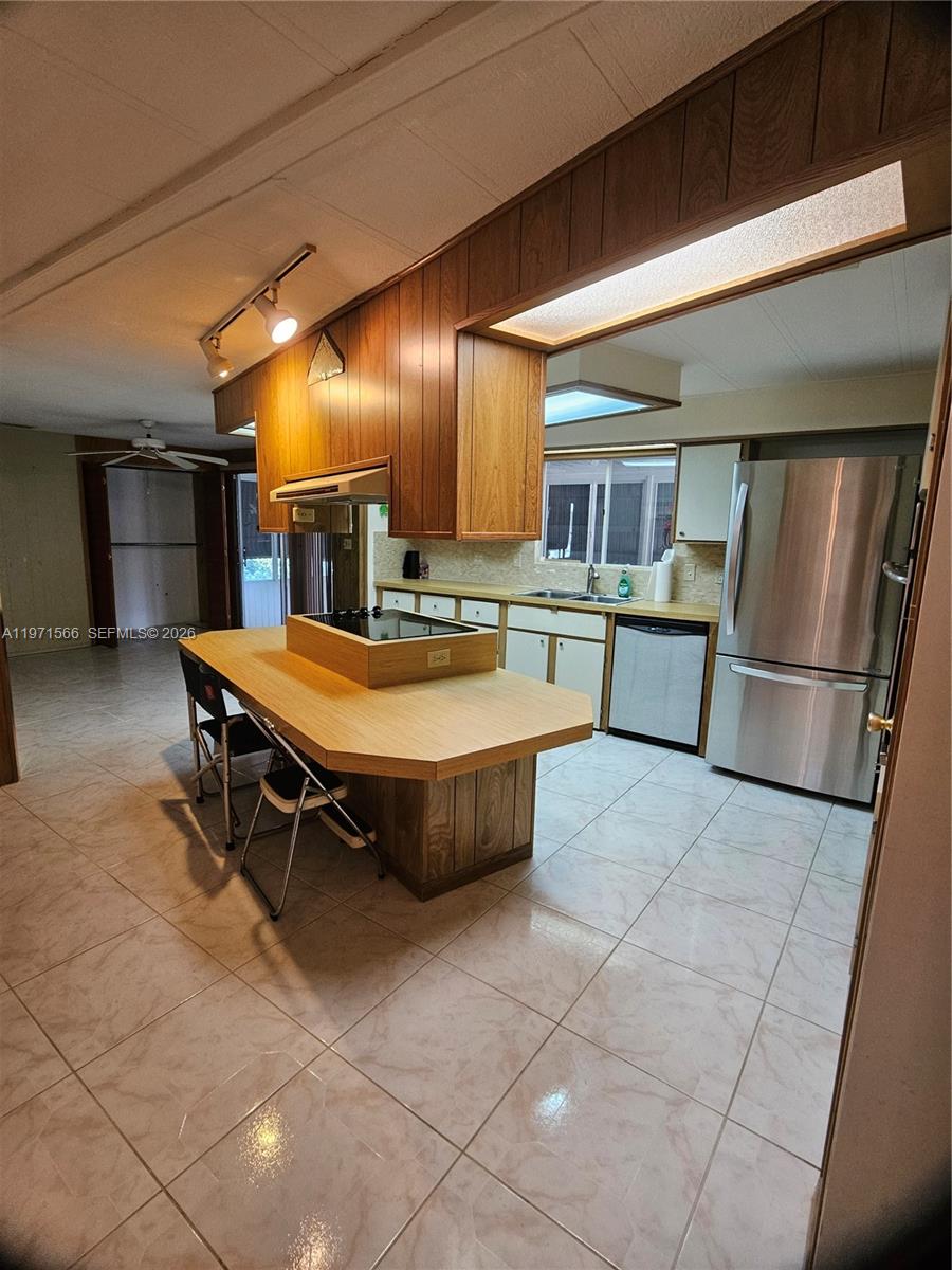A kitchen features wood cabinets, a central island with a cooktop, and stainless steel appliances — 109 NW 51st St, Deerfield Beach FL 33064, DEERFIELD BEACH, FL