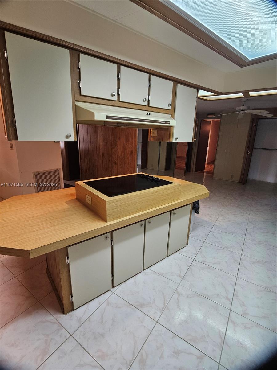 A kitchen features a central island with a cooktop, light wood cabinetry, and tiled flooring — 109 NW 51st St, Deerfield Beach FL 33064, DEERFIELD BEACH, FL