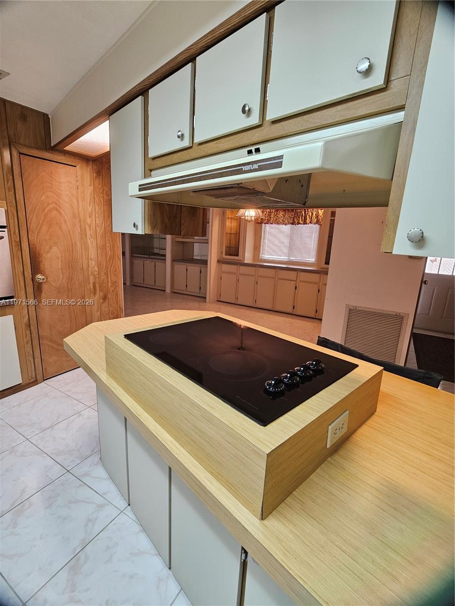 A kitchen features a central island with a cooktop, light wood cabinetry, and tiled flooring — 109 NW 51st St, Deerfield Beach FL 33064, DEERFIELD BEACH, FL