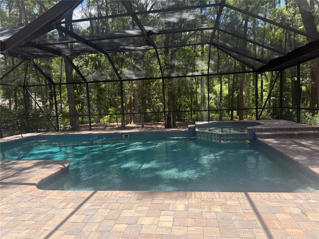A single-story house with a stone facade sits among many trees and a paved driveway — 4427 SW 84TH WAY, GAINESVILLE, FL