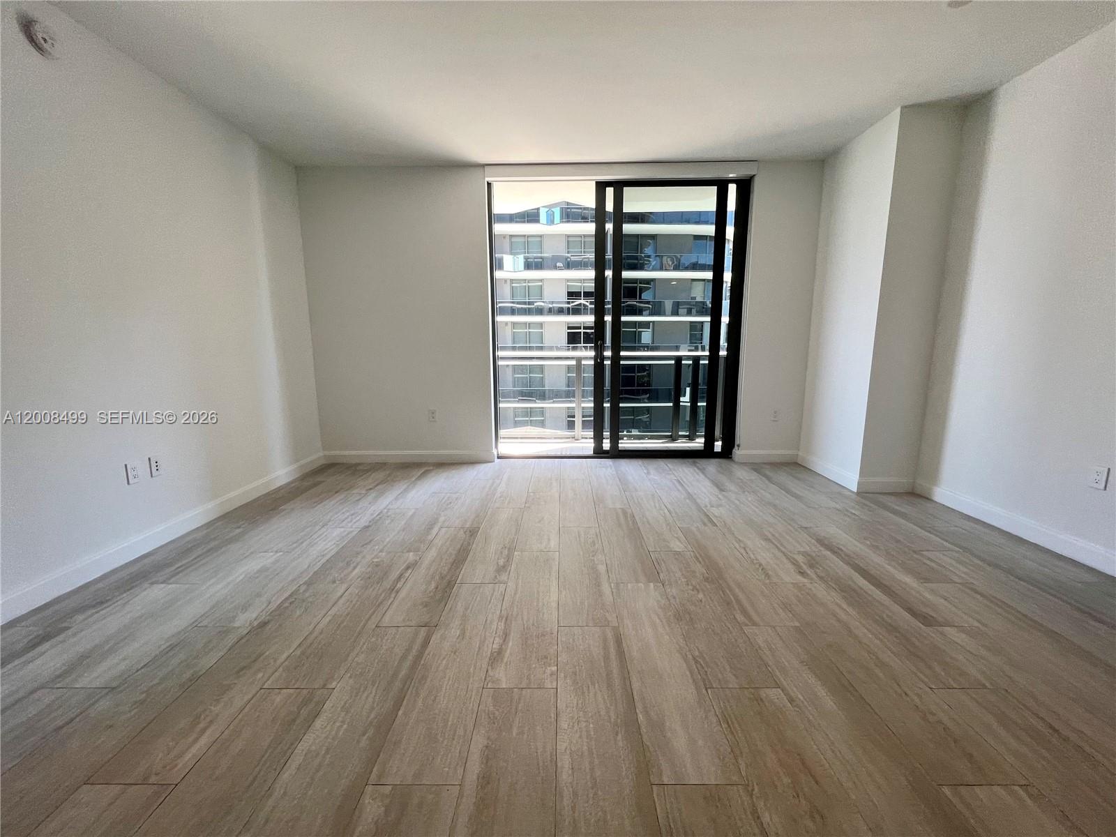 An empty room features light wood-look tile flooring, white walls, and a sliding glass door — 55 SW 9th St # 2702, Miami FL 33130, MIAMI, FL