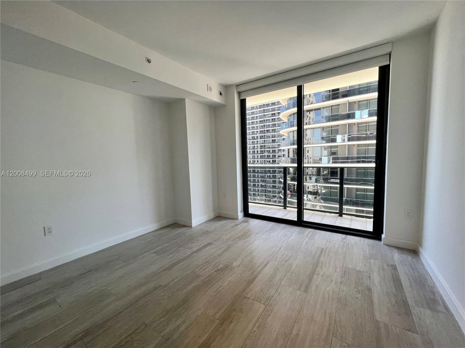 An empty room features light wood-look flooring, white walls, and a large sliding glass door — 55 SW 9th St # 2702, Miami FL 33130, MIAMI, FL