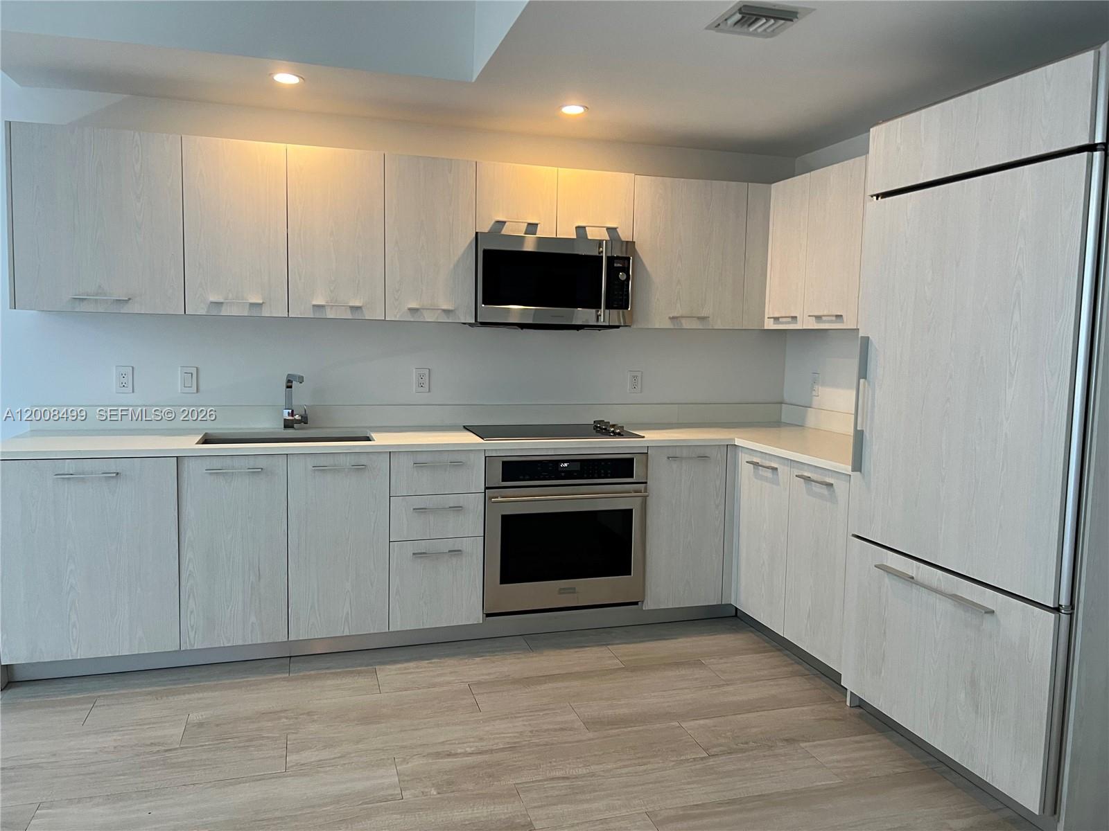 A modern kitchen features light wood-grain cabinets, stainless steel appliances, and white countertops — 55 SW 9th St # 2702, Miami FL 33130, MIAMI, FL