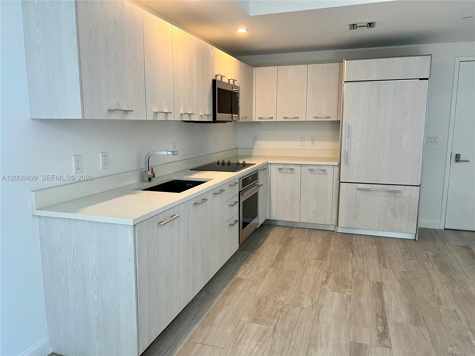A modern kitchen features light wood-grain cabinets, white countertops, and stainless steel appliances — 55 SW 9th St # 2702, Miami FL 33130, MIAMI, FL