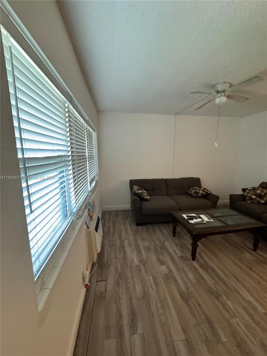 A living room features wood-look flooring, a ceiling fan, and a large window with blinds — 118 E Salisbury  E # 118, West Palm Beach FL 33417, WEST PALM BEACH, FL