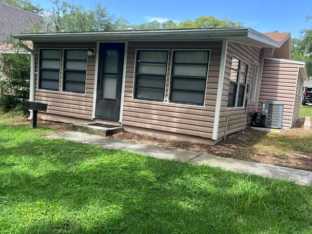 The exterior of a small, tan-sided house features a dark front door and multiple windows — 10301 US HIGHWAY 27 UNIT 182, CLERMONT, FL