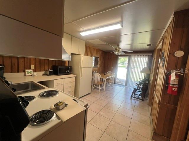 A kitchen with wood-paneled walls, white cabinets, a white refrigerator, and a dining area — 10301 US HIGHWAY 27 UNIT 182, CLERMONT, FL