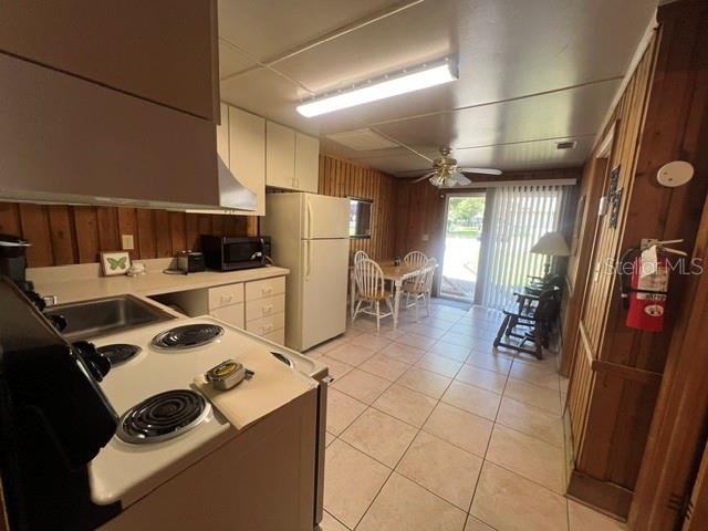 A kitchen with wood-paneled walls, white appliances, and tile flooring leads to a dining area — 10301 US HIGHWAY 27 UNIT 182, CLERMONT, FL