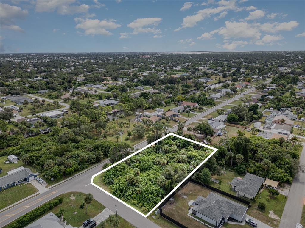 An aerial view shows a vacant, wooded residential lot outlined in white along a paved road — 18503 BARBARA AVENUE, PORT CHARLOTTE, FL