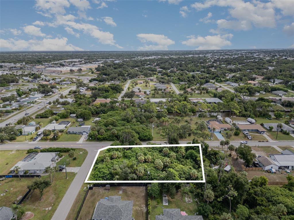 An aerial view shows a vacant, rectangular lot covered in dense vegetation and palm trees — 18503 BARBARA AVENUE, PORT CHARLOTTE, FL