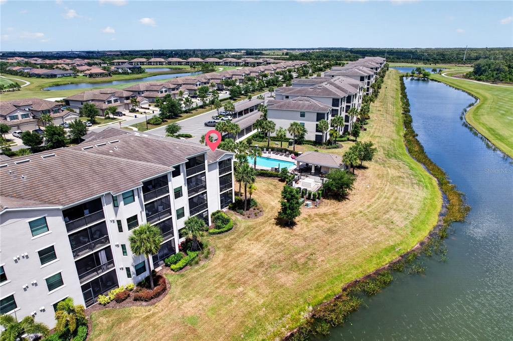 An aerial view shows a multi-story apartment building next to a swimming pool and lake — 17724 GAWTHROP DRIVE UNIT 301, BRADENTON, FL