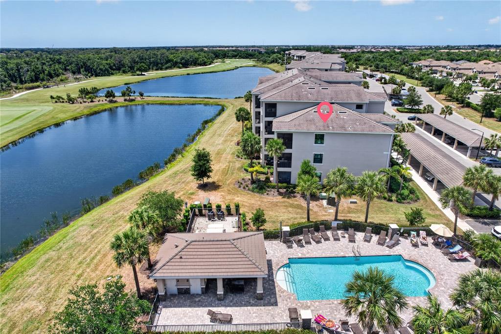 An aerial view shows a multi-story apartment building next to a pool and lake — 17724 GAWTHROP DRIVE UNIT 301, BRADENTON, FL