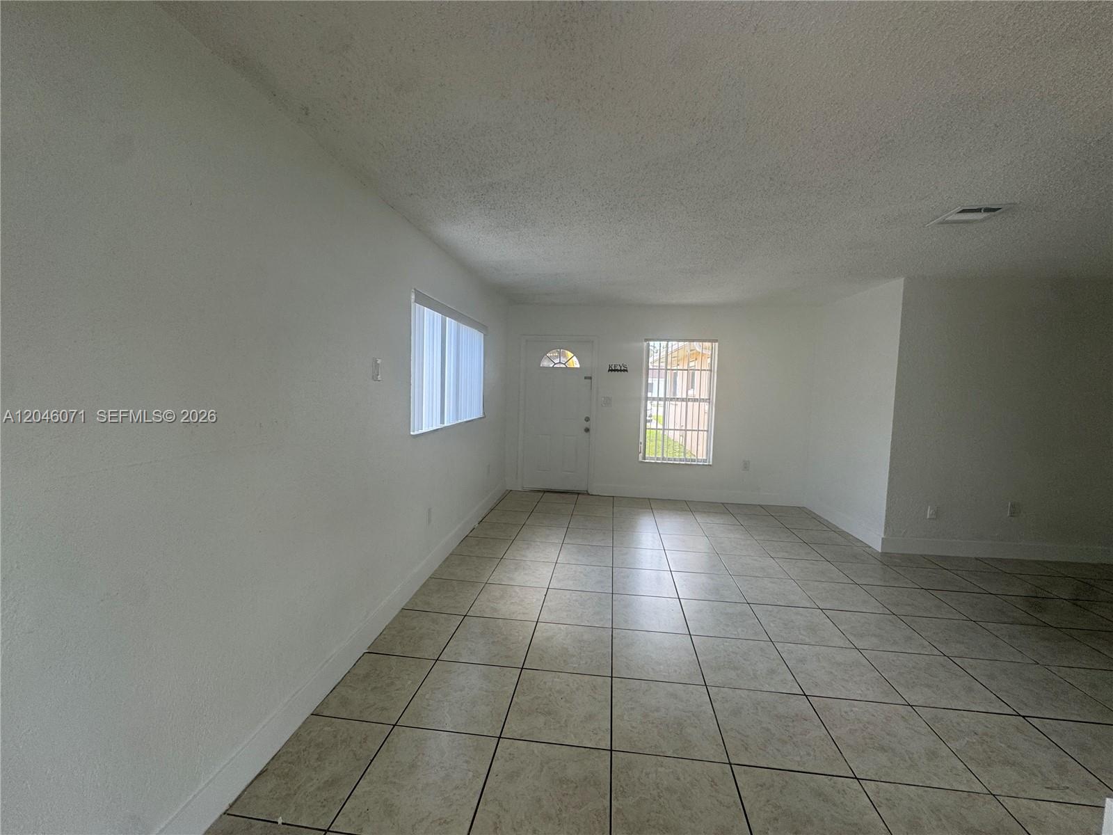 An empty room features white walls, light-colored tile flooring, a front door, and two windows — 3810 SW 89th Ave # 3810, Miami FL 33165, MIAMI, FL