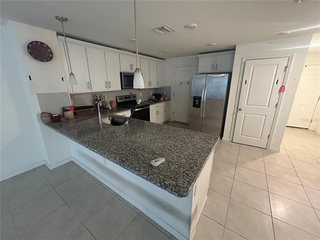 A kitchen features white cabinets, granite countertops, a stainless steel refrigerator, and tile flooring — 15031 CASPIAN TERN COURT UNIT 103, NORTH FORT MYERS, FL