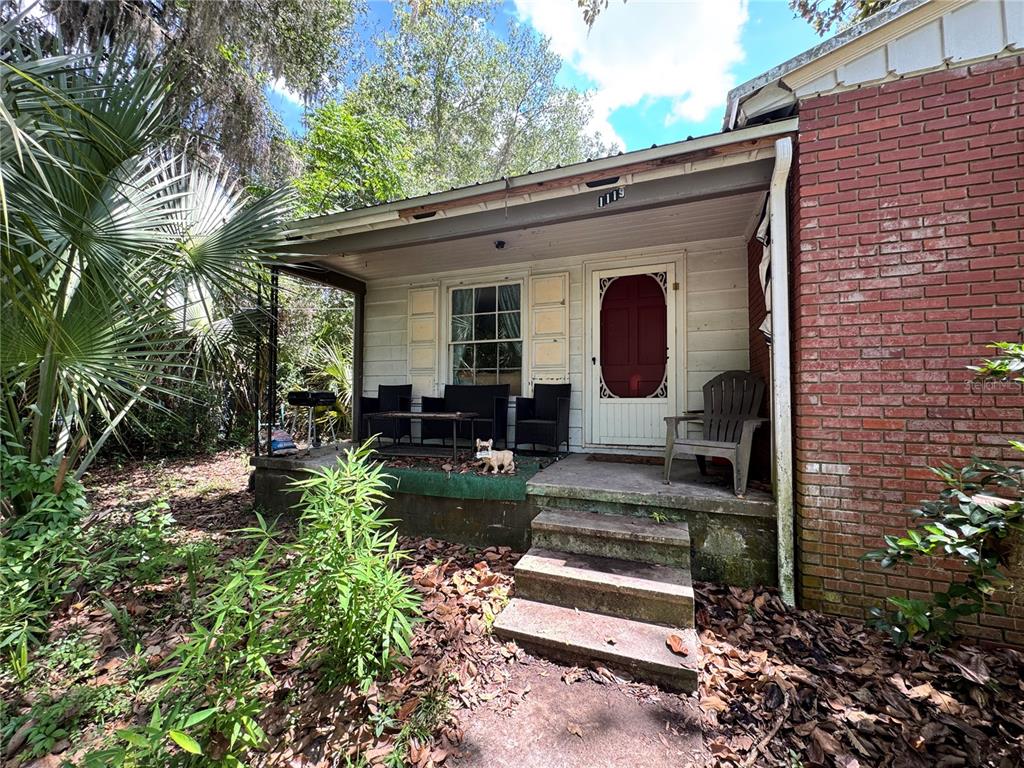A brick house features a covered front porch with concrete steps and outdoor furniture — 1119 NW 25TH AVENUE, GAINESVILLE, FL