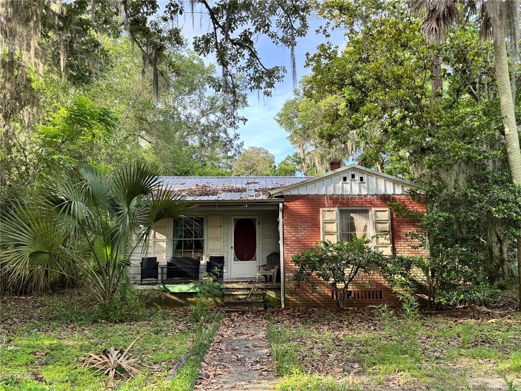 A one-story brick and wood-sided house sits surrounded by trees with a metal roof — 1119 NW 25TH AVENUE, GAINESVILLE, FL