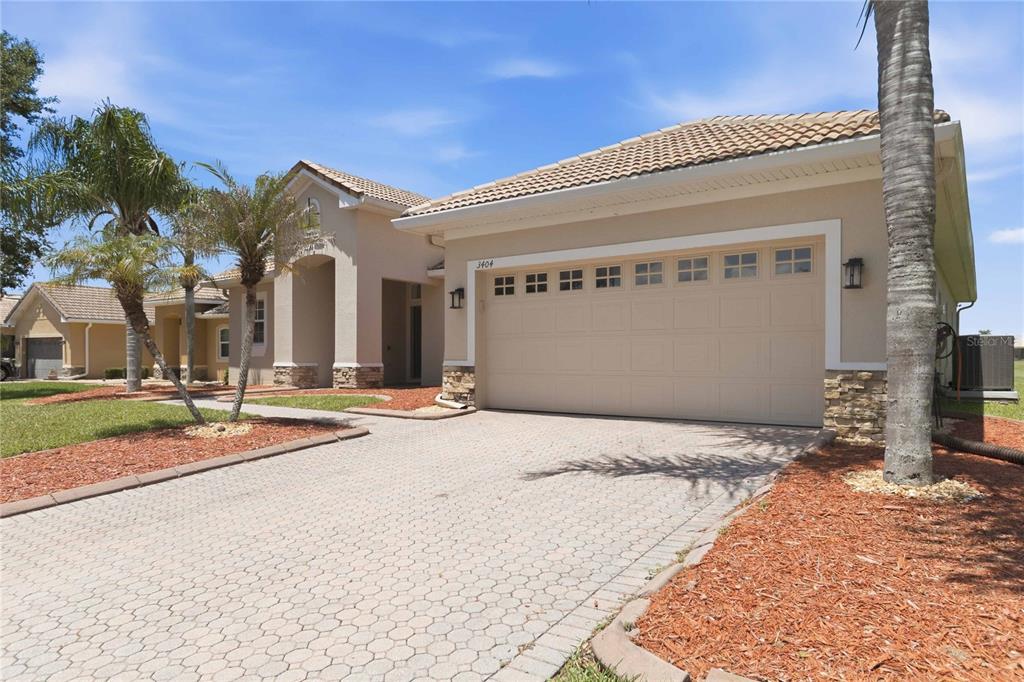 A beige single-story house with a paver driveway, a two-car garage, and palm trees — 3404 GREAT POND DRIVE, KISSIMMEE, FL