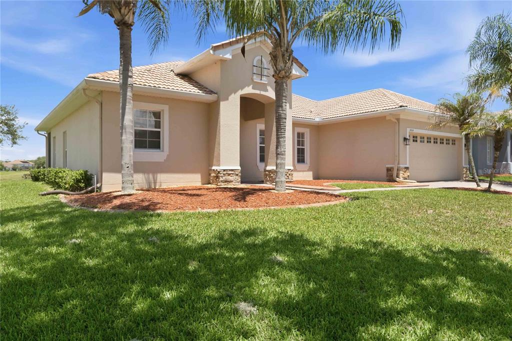 A single-story beige stucco house with a tiled roof, palm trees, and a two-car garage — 3404 GREAT POND DRIVE, KISSIMMEE, FL