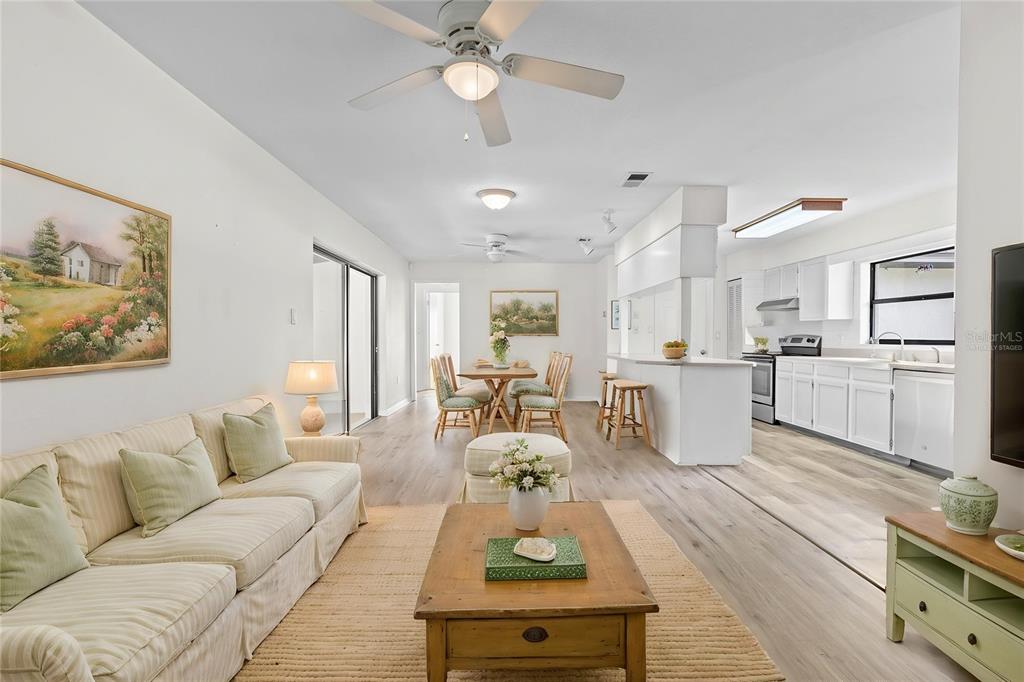 An open-concept living room, dining area, and kitchen with light wood-look flooring and white cabinetry — 2707 BALKAN STREET, APOPKA, FL