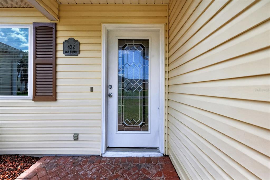A white front door with a decorative glass insert sits beside yellow horizontal siding — 422 SAN MARINO DRIVE, THE VILLAGES, FL