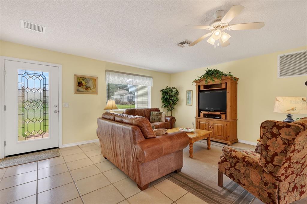 A living room features tile flooring, a leather sofa, a floral armchair, and a ceiling fan — 422 SAN MARINO DRIVE, THE VILLAGES, FL