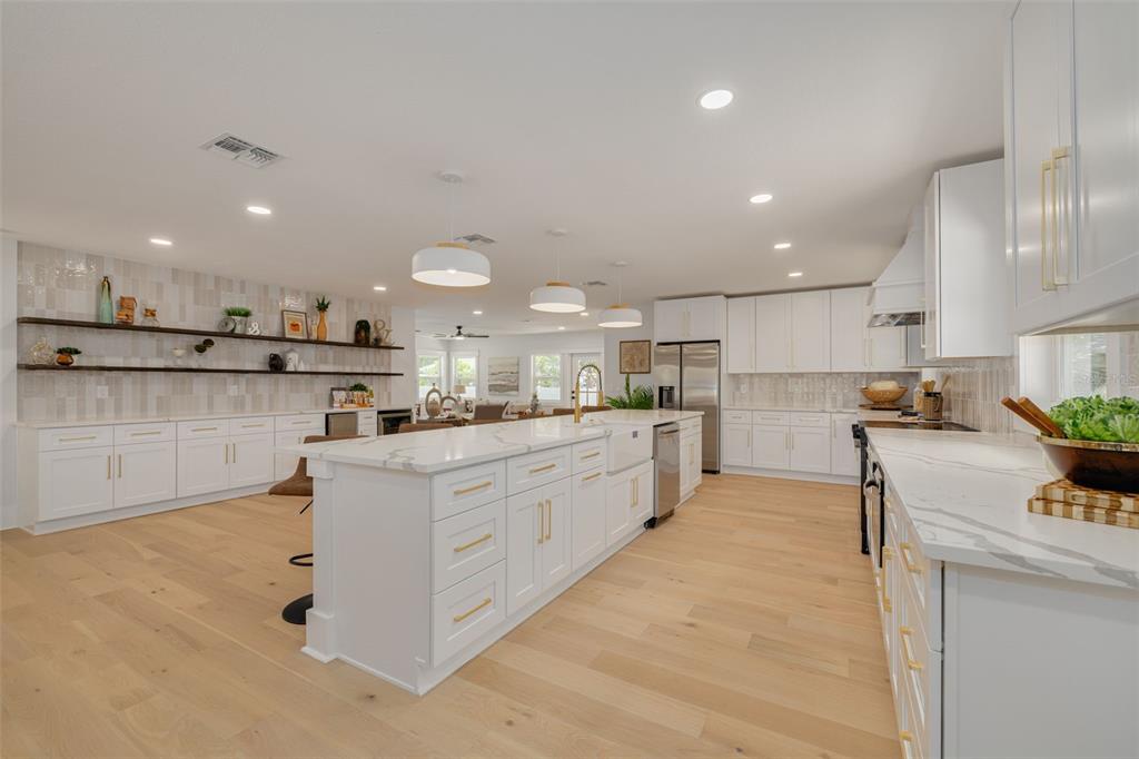 A modern white kitchen features a large marble-topped island, open shelving, and light wood flooring — 1426 15TH STREET N, ST PETERSBURG, FL