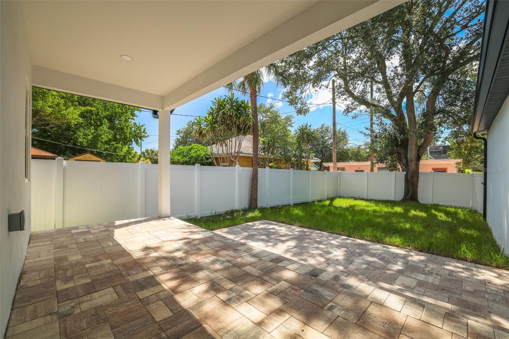 A covered patio with paver flooring overlooks a small backyard enclosed by a white fence — 1426 15TH STREET N, ST PETERSBURG, FL