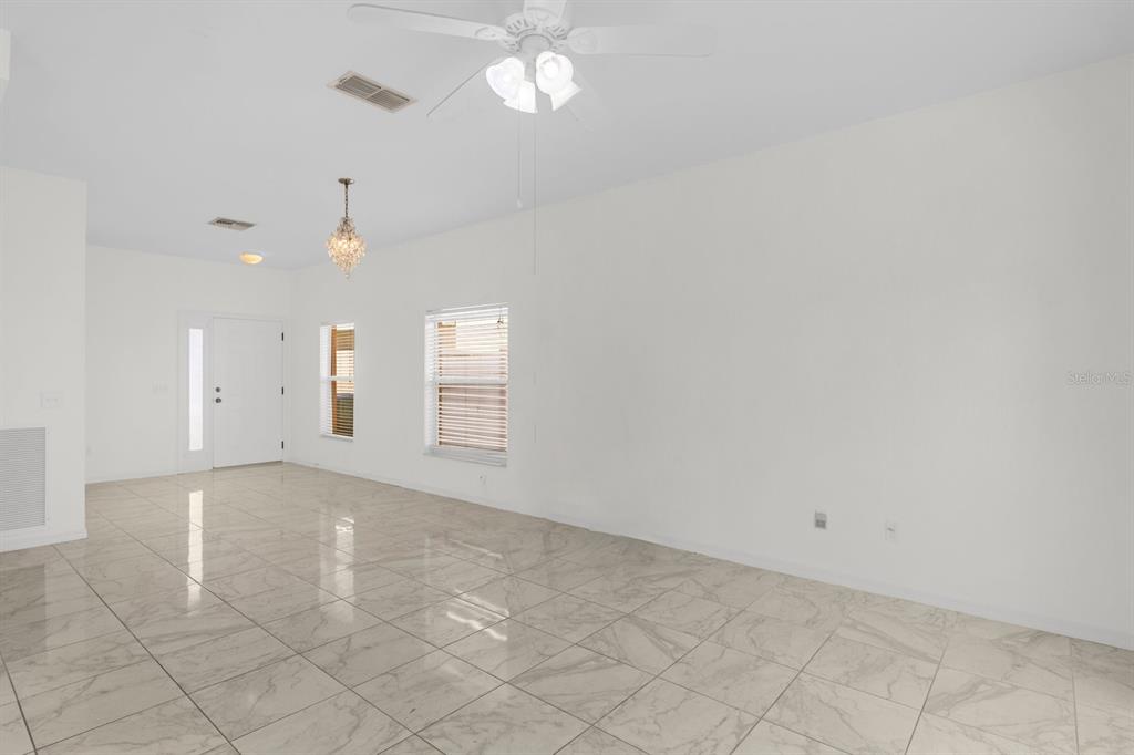 An empty room with white walls, tile flooring, a ceiling fan, and a crystal chandelier — 5090 NE 122ND BOULEVARD, OXFORD, FL
