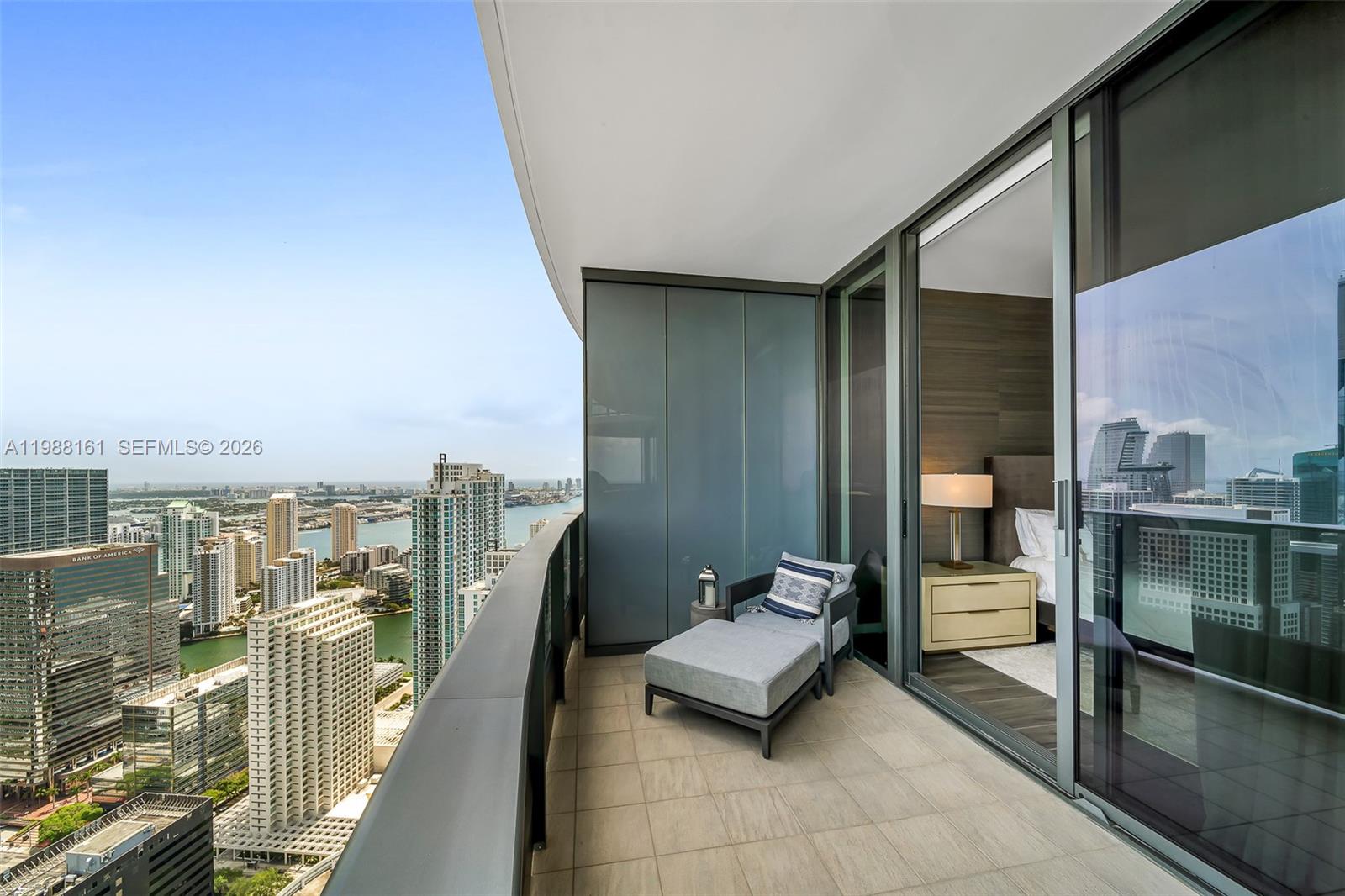 A high-rise balcony features a lounge chair and sliding glass doors overlooking a city skyline — 1000 Brickell Plz, Miami FL 33131, MIAMI, FL