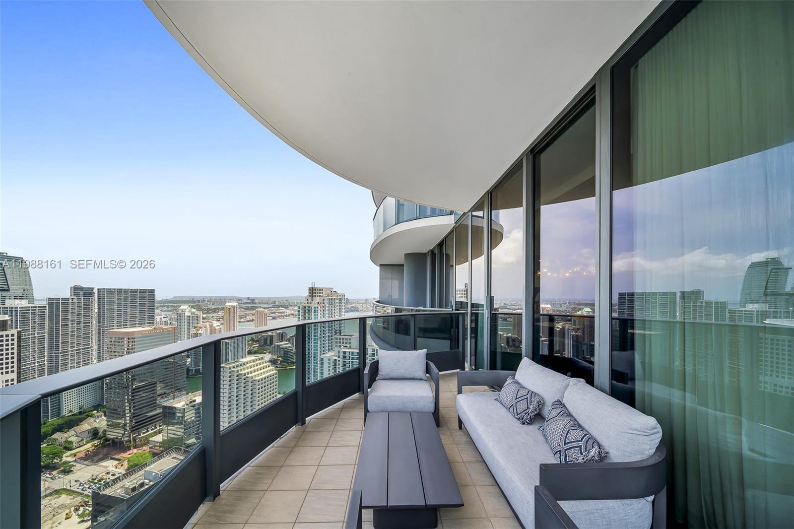 A high-rise balcony features outdoor seating, a coffee table, and panoramic city and water views — 1000 Brickell Plz, Miami FL 33131, MIAMI, FL
