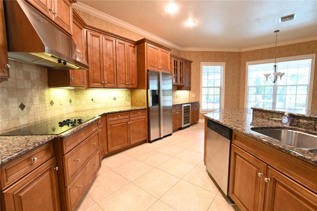 A kitchen features wood cabinets, granite countertops, stainless steel appliances, and tile flooring — 8122 WHITFORD COURT, WINDERMERE, FL