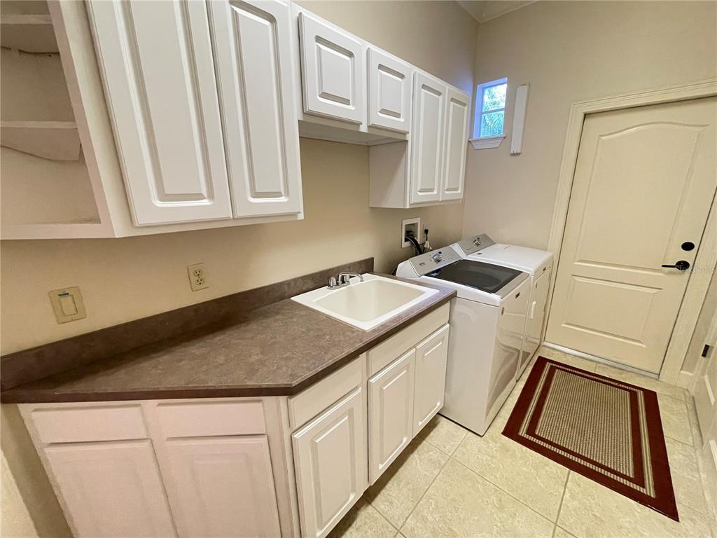 A laundry room features white cabinets, a utility sink, and a washer and dryer set — 8122 WHITFORD COURT, WINDERMERE, FL