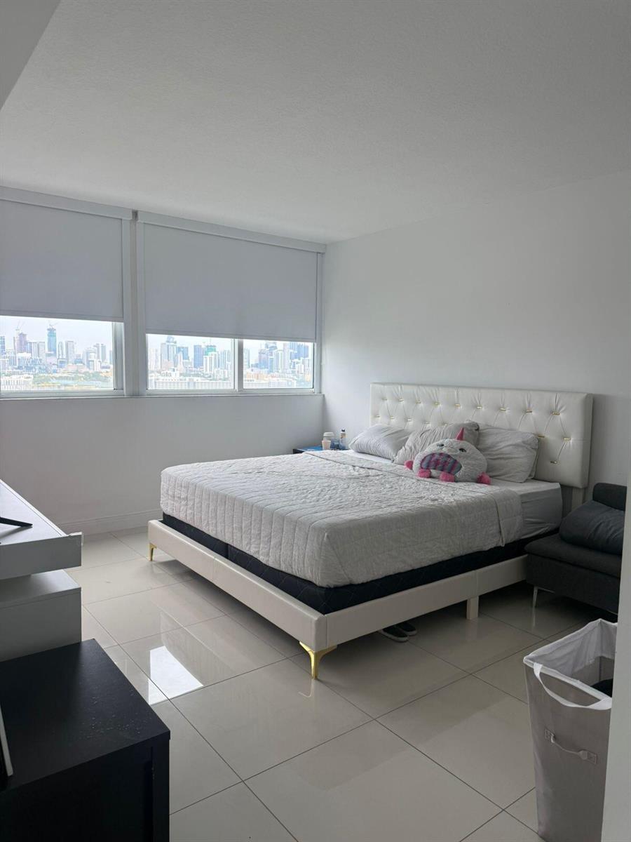 A bedroom features a white tufted bed, tile flooring, and large windows with city views — 1861 NW S River Drive # 2408, Miami FL 33125, MIAMI, FL