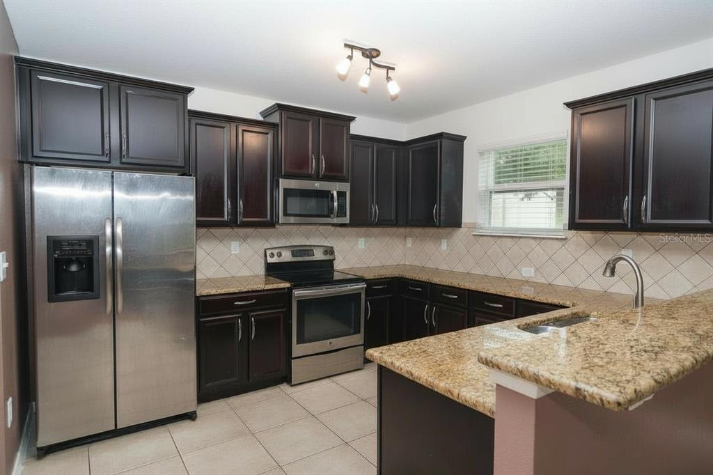 A kitchen with dark wood cabinets, granite countertops, stainless steel appliances, and tile flooring — 5909 WINDSONG OAK DRIVE, LEESBURG, FL