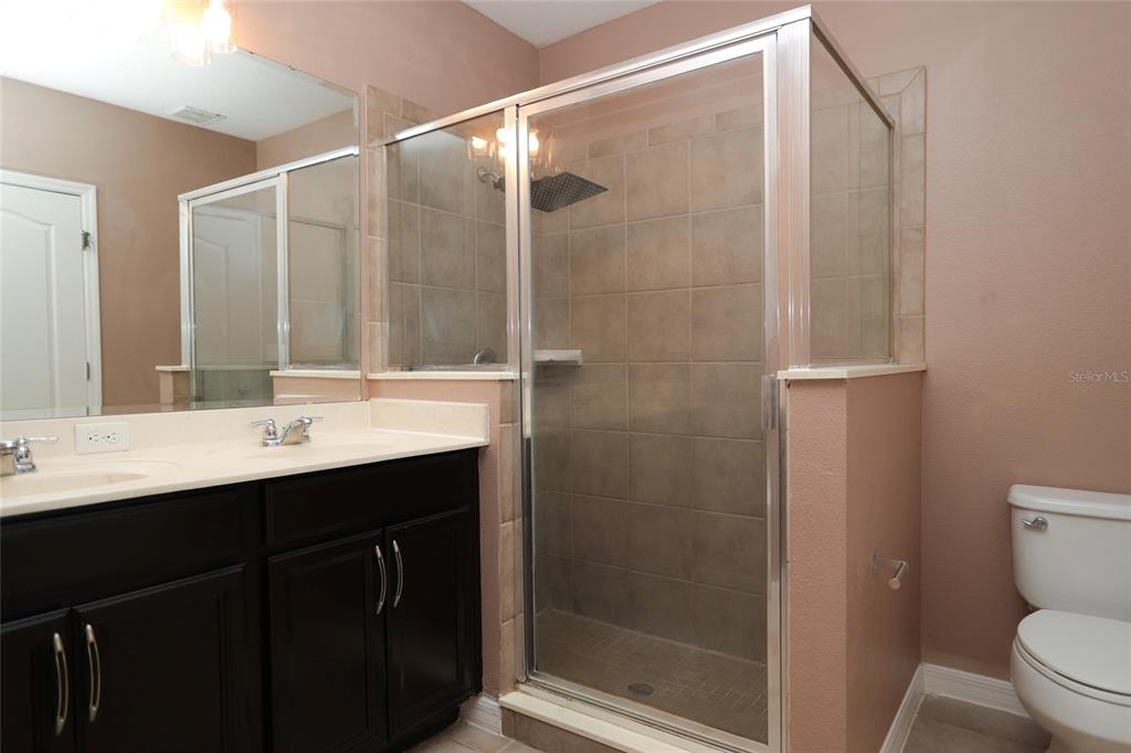 A bathroom features a dark wood vanity, a glass-enclosed tiled shower, and a white toilet — 5909 WINDSONG OAK DRIVE, LEESBURG, FL