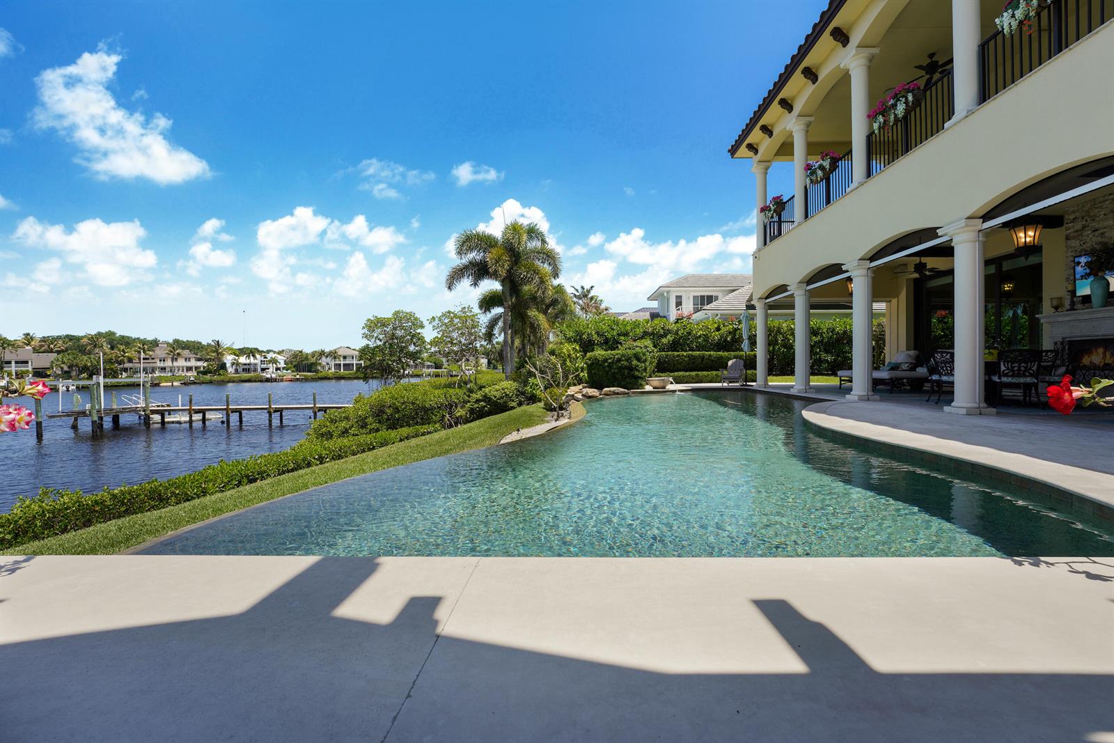 An infinity pool overlooks a canal with a dock next to a two-story waterfront home — 10433 SE Banyan Way, Jupiter FL 33469, JUPITER, FL
