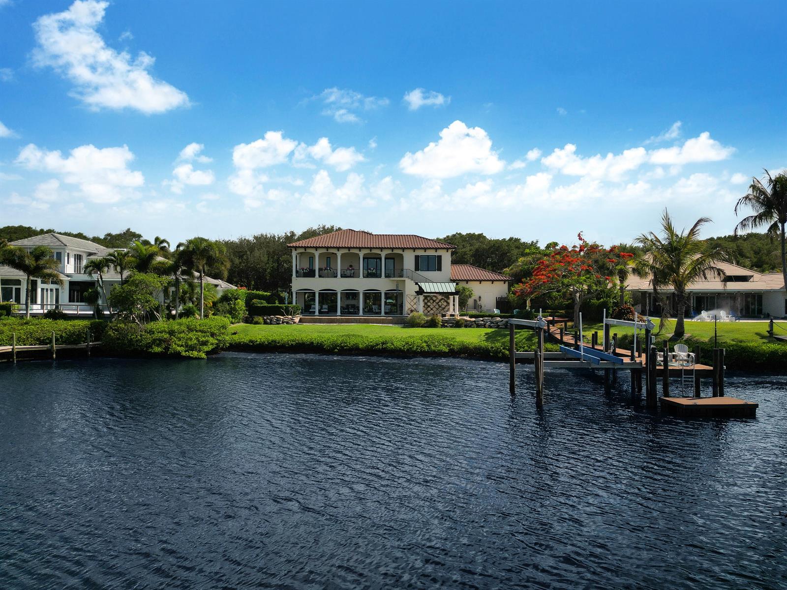 A two-story waterfront house with a private dock sits along a canal under a blue sky — 10433 SE Banyan Way, Jupiter FL 33469, JUPITER, FL