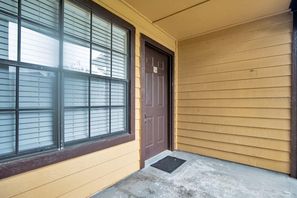 A brown front door is set into a yellow-sided exterior wall next to a window — 360 LAKE ONTARIO COURT UNIT 104, ALTAMONTE SPRINGS, FL