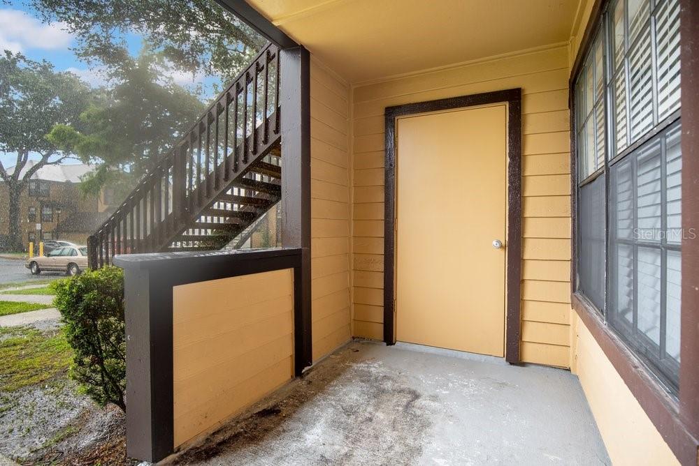 An exterior view of a covered apartment entryway with a yellow door and wooden stairs — 360 LAKE ONTARIO COURT UNIT 104, ALTAMONTE SPRINGS, FL