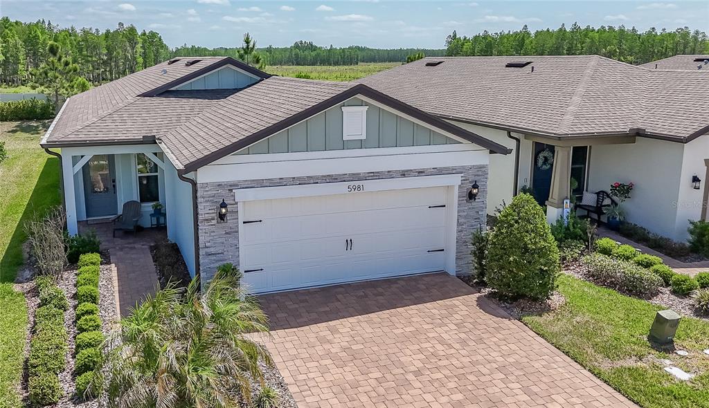 An exterior view of a single-story house featuring a stone-accented garage and paver driveway — 5981 SHOREBIRD BRANCH, LAND O LAKES, FL