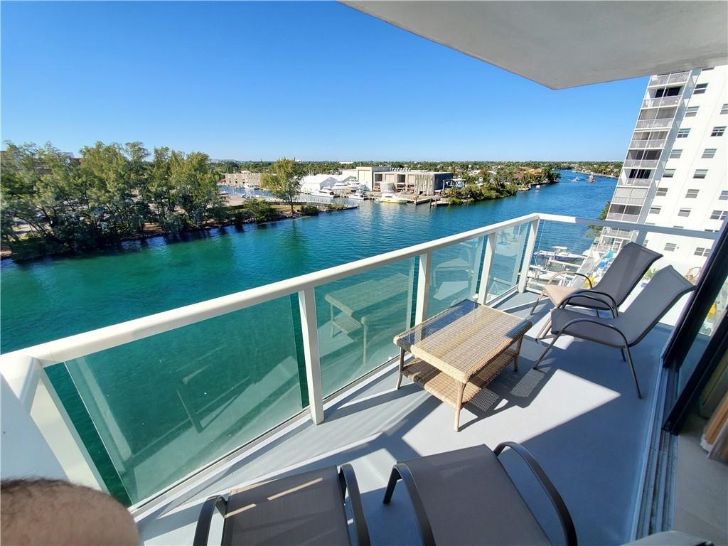 A balcony with outdoor furniture overlooks a canal and a nearby high-rise building — 1401 N Riverside Drive N # 807, Pompano Beach FL 33062, POMPANO BEACH, FL