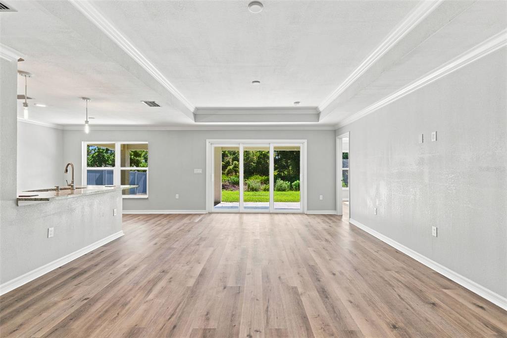 An open-concept living area features light wood-look flooring, a tray ceiling, and sliding glass doors — 12263 CARTOUCHE AVENUE, PUNTA GORDA, FL