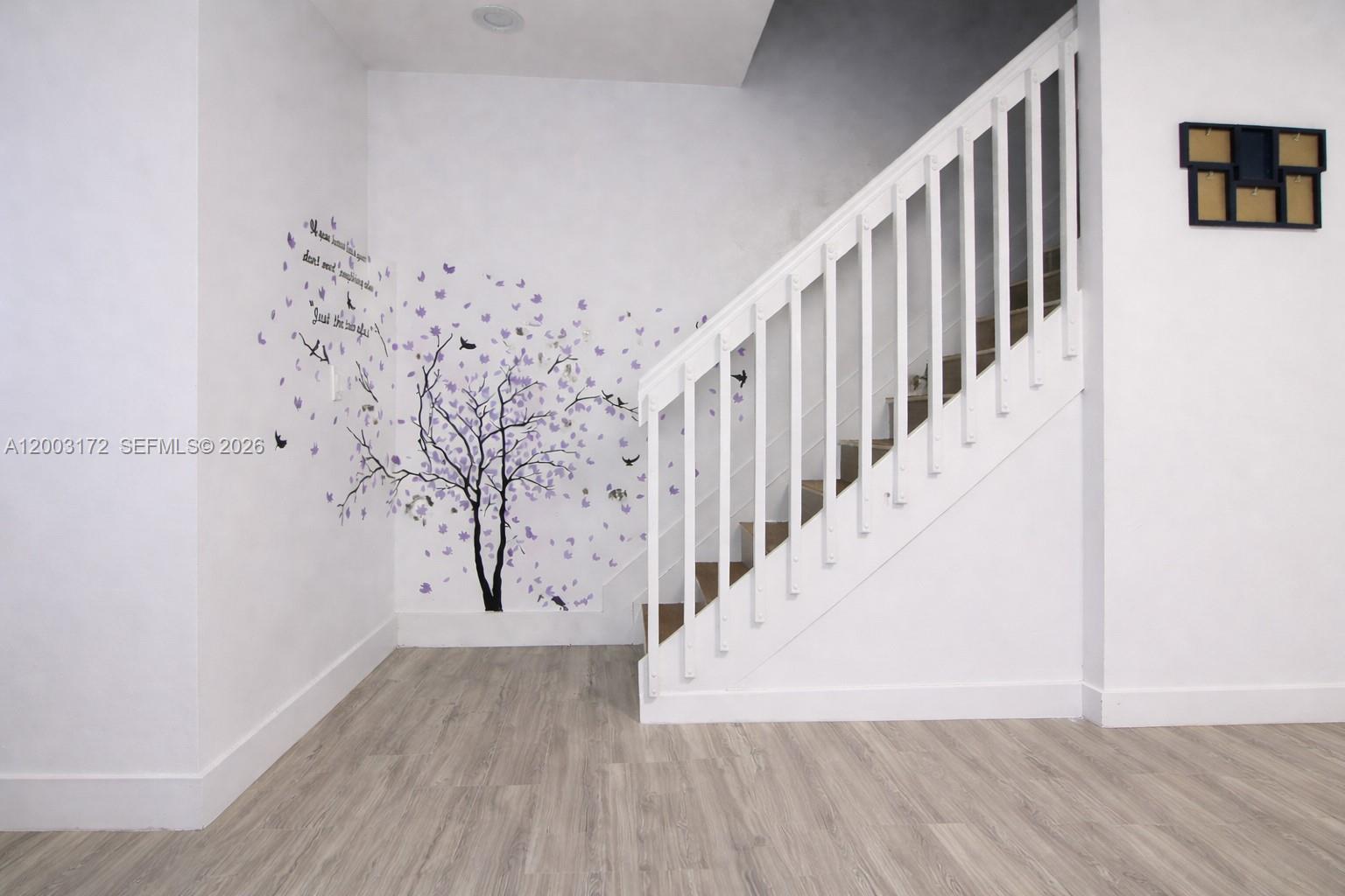 A staircase with white railings stands next to a wall decorated with a tree decal — 2264 NE 42nd Cir, Homestead FL 33033, HOMESTEAD, FL
